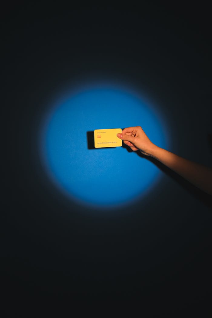 A hand holds a yellow card under spotlight against a dark backdrop, emphasizing mystery.